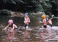川の浅瀬で楽しそうに遊ぶ4人の水着姿の子どもたちの写真