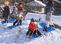 子どもたちがそりで雪の上をすべる様子の写真