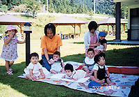 女性二名と子どもたちが芝生にひいたレジャーシートに座っている写真