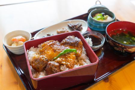 吸い物や小鉢などが付き、正方形の朱色の重箱に詰められたご飯の上にチョウザメとタレがかかった「ザメ重」の写真