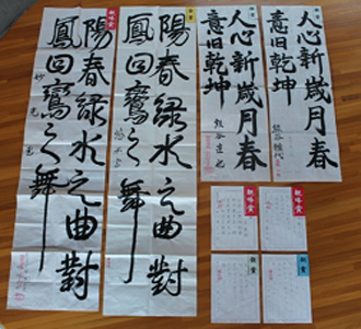床に並べられている長い半紙に書かれた習字の作品4点、ペン字の作品4点の写真