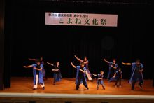 「とよね文化祭」と書かれた横断幕が掲げられたステージ上に長めの紫の法被を着た大人、子供たちが踊っている写真