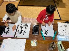 2人の小学生が習字の練習をしている姿を前から撮影した写真