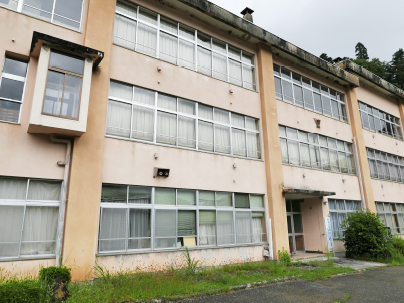 ベージュを基調とした3階建ての校舎の前に小さな木が植えられている旧豊根小学校の写真