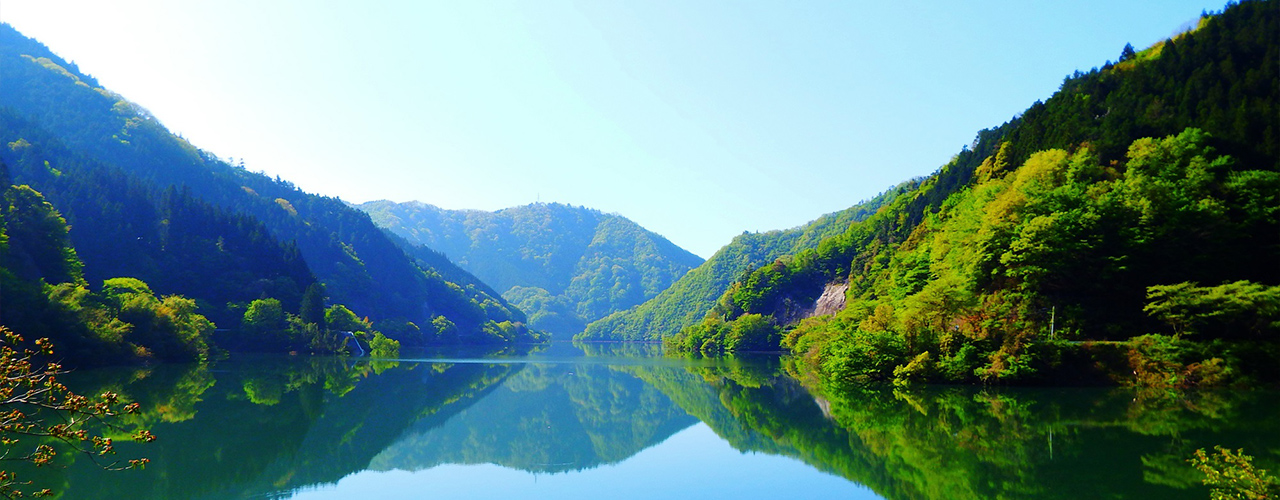 三方の山に囲まれ水面に生い茂った木々が反射して写っているみどり湖の写真