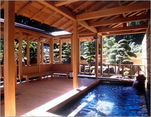 屋根付きでベンチなどが備え付けられており、外には選定された松の木などの自然が見える露天風呂の写真