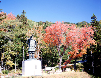 紅葉などたくさんの木々の周りに建っている尹良親王像の写真